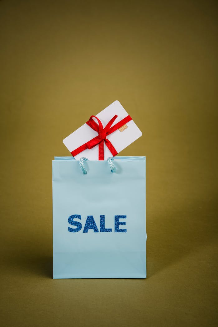 A gift card tied with a red bow on a blue shopping bag with 'SALE' text, perfect for promotional use.